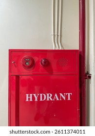 A red fire hydrant box mounted on a wall, equipped with a fire alarm button and indicator light, designed for emergency fire protection in buildings.