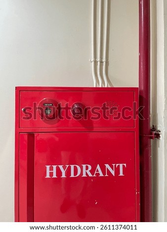 A red fire hydrant box mounted on a wall, equipped with a fire alarm button and indicator light, designed for emergency fire protection in buildings.