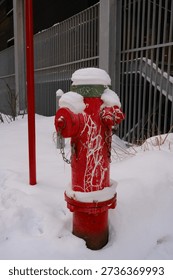 A red fire hydrant capped with fresh snow stands against a metal fence in a quiet winter streetscape