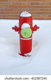Red fire hydrant covered by snow, near a brick building.