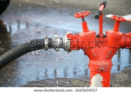 A red fire hydrant with a hose attached that supplies water.                               