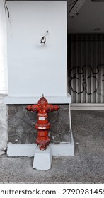 Red fire hydrant installed on a sidewalk next to a building wall