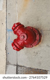 A red fire hydrant is positioned on a concrete sidewalk in an urban area. The hydrant shows signs of wear and is surrounded by gray pavement with a few colorful markings.