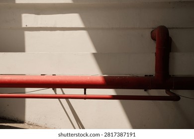 Red fire hydrant or sprinkler system pipes installed along the wall of an Indonesian public building, photographed with natural sunlight coming through a window. Industrial infrastructure for fire safety and emergency response in commercial or government buildings. Ideal for industrial and safety stock photography.