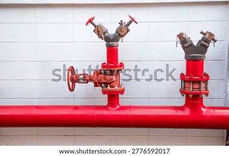 Red fire hydrant system pipes and valves installed on a white concrete wall outside a building,Industrial fire protection system with red pipes, valves, and water supply connection for emergency safety.