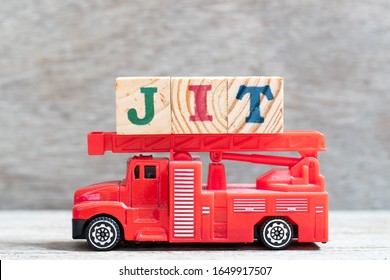 Red fire truck hold letter block in word JIT (abbreviation of just in time) on wood background