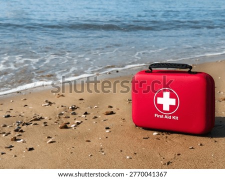Red first aid kit placed on sandy beach near sea waves emergency medical equipment for travel safety health insurance concept outdoor vacation preparedness copyspace.