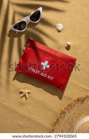 Red first aid kit placed on warm sand beside sunglasses and straw hat highlighting health, safety and emergency preparedness for beach vacation and travel