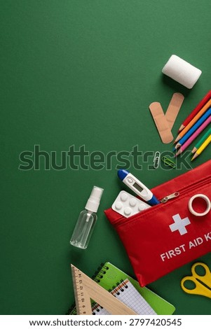 Red first aid kit with thermometer, tablet, spray and bandage beside school supply on green background conveying student health safety and preparedness