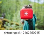 A red first aid kit with a white cross is held outdoors, symbolizing emergency preparedness and safety during nature activities. Essential for backcountry adventures, travel, and exploration