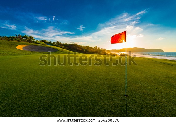 Red flag at the beautiful golf course at\
the ocean side at sunset, sunrise\
time.