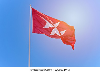 Red flag with black cross. Symbol of the Knights of Malta is the eight-pointed cross in sunrise against blue sky, copy space