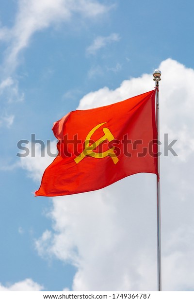 A red flag with communist symbols of a sickle\
with a hammer flying in a blue\
sky