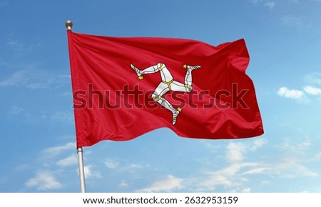 Red flag of the Isle of Man featuring a triskelion of three armored legs, flying against a blue sky background.