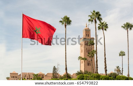 Red flag with palms from Morocco and Djemma el Fna tower. Touristic place in Marrakesh used by local people as square or market place. Emblematic landscape - traditional building from arabic culture.