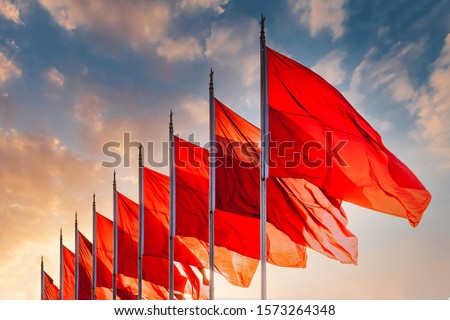 Red flags, the symbol of the Chinese communist party blow in the wind in the center of Beijing Tiananmen Square. Sunset sky in background with no recognisable buildings. 
