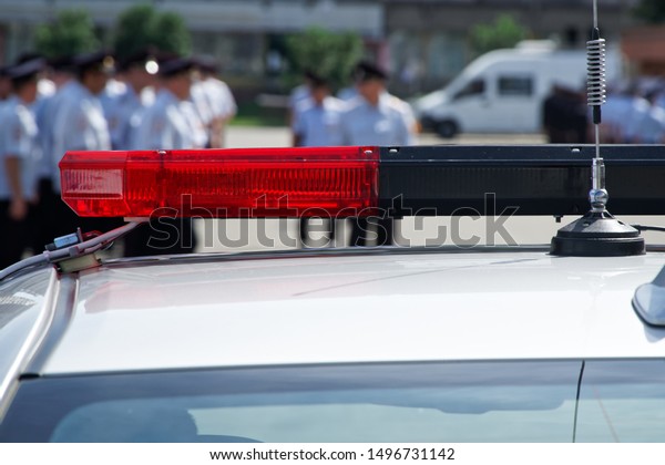 Red flashing light and antenna of a police car\
on a city street. Daylight