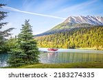 Red float plane parked on the waters of Upper Trail Lake on the Kenai Peninsula of Alaska USA framed by pine trees with blurred mountains with snow above the tree line in the background