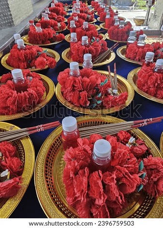 Red flower offerings, incense sticks and red water in a golden tray. 