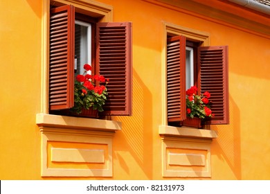 Red flowers on the windowsills of a yellow house