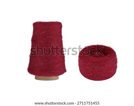 A Red fluffy yarn set with a spool on a cardboard bobbin and a smaller ball, isolated on a white background. Ideal for knitting, crocheting, or craft projects, this fresh yarn adds a cool,