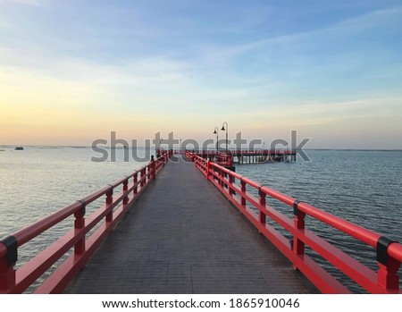 a red foot bridge leads to the blue sea with colorful sunset background.