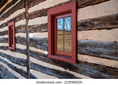 A Red Four-pane Window Reflects A Rural Landscape In The Exterior Wall Of An Early American Colonial Log Cabin. Wood Texture And Long Striped Lines With Red Windows. Natural Light, No People.