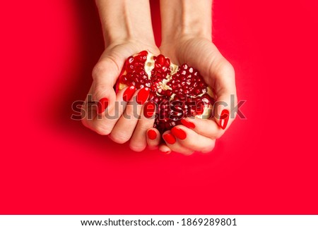 Red fresh pomegranate in woman's hand, fingernails with red nail polish on red background. Close up.