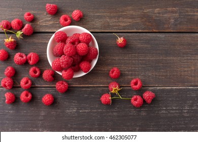 Red fresh raspberries on brown rustic wood background. Bowl with natural ripe organic berries with peduncles on wooden table, top view with copy space
