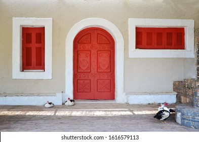 Red Front Door Of House And Window With Wooden Shutter. Old Facade Achitecture In Vintage Style. Close Up And Background.