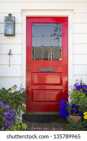 Red Front Door Of An Upscale Home/Vertical Shot Of A Red Front Door On A Home With A Mail Slot, Plants, Doorbell, Brick Flooring And Reflection In The Window.