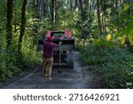 Red front loader tractor with load of fresh gravel delivering it to a forest path in public park, workman with shovel guiding the equipment operator, maintenance team hard at work
