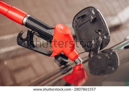 Red fuel nozzle inserted into a car gas tank at a petrol station close-up, fuel refilling and transport economy concept. High quality photo
