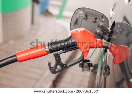 Red fuel nozzle inserted into a car gas tank at a petrol station close-up, fuel refilling and transport economy concept. High quality photo