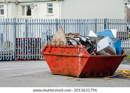 Red garbage removal skip full of rubbish and ready for collection in a street. Old dumpster full of junk in a yard. Waste industry in urban enviroment