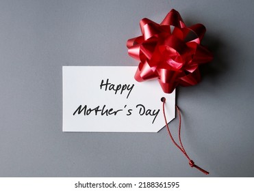 Red gift bow on handwritten text gift tag Happy Mother's Day, refers to celebration honoring the mother or motherhood, to thank for all she's done and wish mom happiness