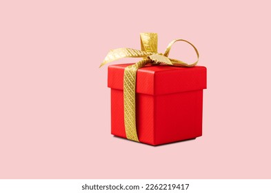 A red gift box with a gold ribbon on a pink background without shadow. The concept of holiday photography. Surprise for Valentine's Day, birthday, wedding. Copy space and front view.