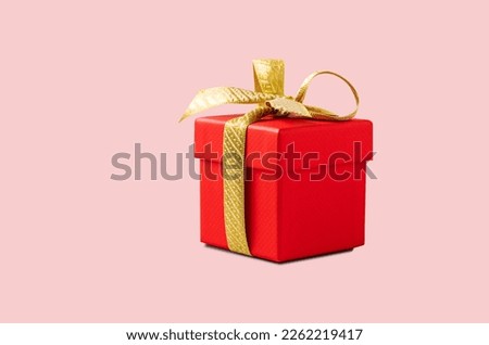 A red gift box with a gold ribbon on a pink background without shadow. The concept of holiday photography. Surprise for Valentine's Day, birthday, wedding. Copy space and front view.