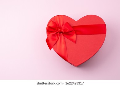 Red gift box heart-shaped on light pink table. Romantic background for Valentine Day or Birthday. Top view. Space for text. 