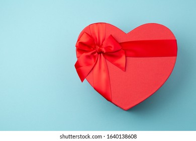 Red gift box heart-shaped on light blue table. Romantic background for Valentine Day or Birthday. Top view. Space for text. 