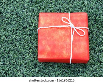 Red gift box on green grass background.Top view. - Powered by Shutterstock