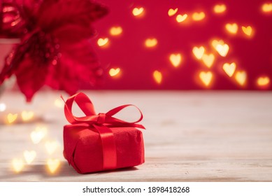 Red gift box on the table with hearts lights garland bokeh with copy space for valentine's day celebration with red colored background. Holiday, love and dating concept.