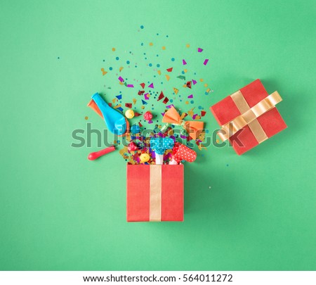 Red gift box with various party confetti, balloons, streamers, noisemakers and decoration on a green background. Colorful celebration background. Flat lay.
