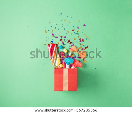 Red gift box with various party confetti, balloons, streamers, noisemakers and decoration on a green background. Flat lay