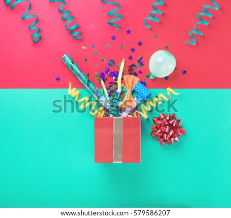 Red gift box with various party confetti, balloons, streamers, noisemakers and decoration on a multicolored background. Top view