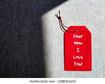 Red gift tag on copy space gray background with handwritten text DEAR MOM I LOVE YOU, concept of Happy Mother's Day card, honoring mother or to thank for all she's done and wish mom happiness