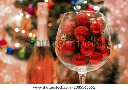 red glitter balls in a large wine glass close up against the background of a decorated green Christmas tree