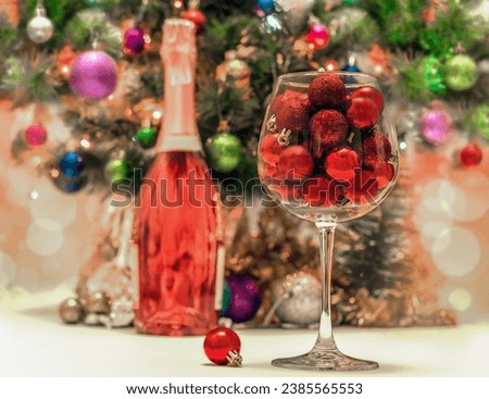 red glitter balls in a large wine glass against the background of a decorated green Christmas tree