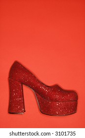 Red glitter high heel shoe against red background.