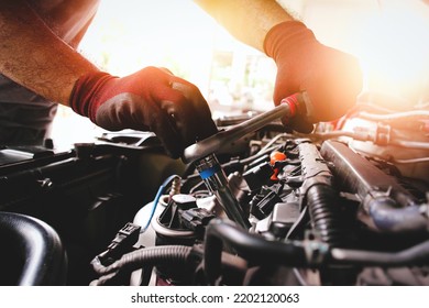 The red gloved hand of the auto mechanic is fastening the bolt with the socket wrench to fix the vehicle engine, sunlight on background - Shutterstock ID 2202120063